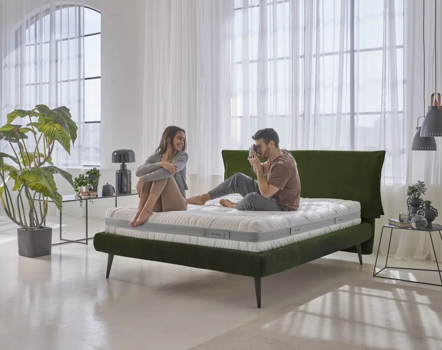 A couple relaxing on a Dorelan Evoke mattress with a green bed frame, set in a bright, modern bedroom filled with natural light and stylish decor.