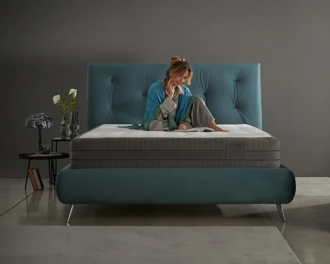 Woman sitting comfortably on a luxurious Dorelan mattress with an elegant teal bed frame