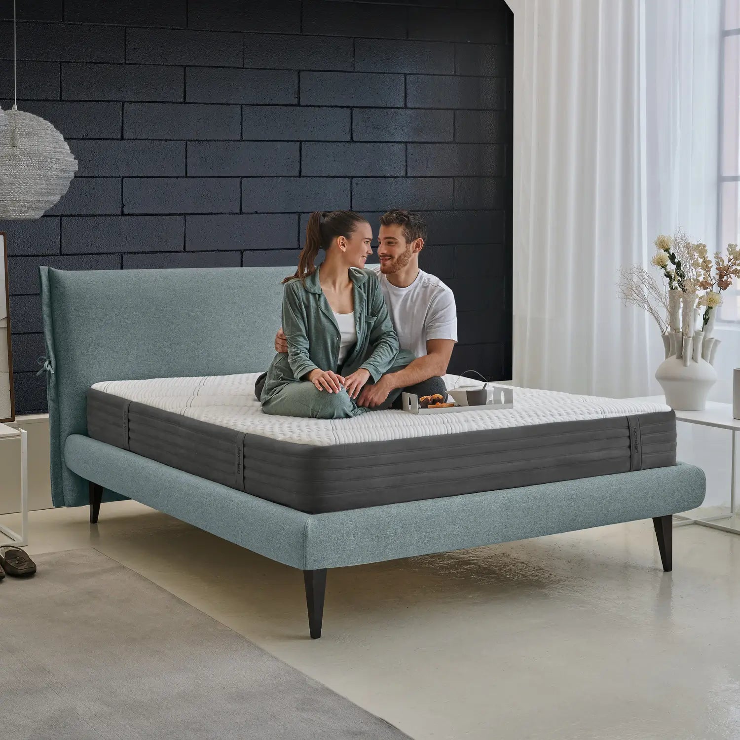 A couple sitting on a Dorelan Nube mattress with a teal bed frame, sharing a cozy moment in a stylish bedroom.