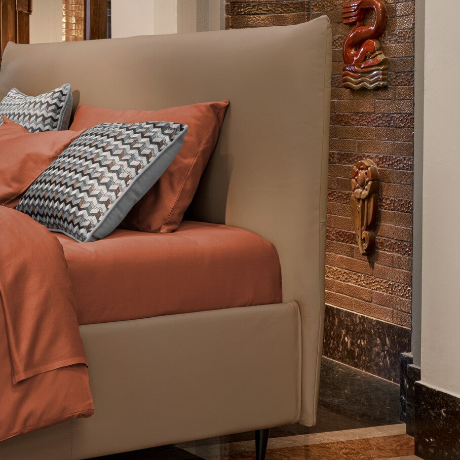 letto imbottito con testiera compatta color beige sabbia e lenzuola arancioni