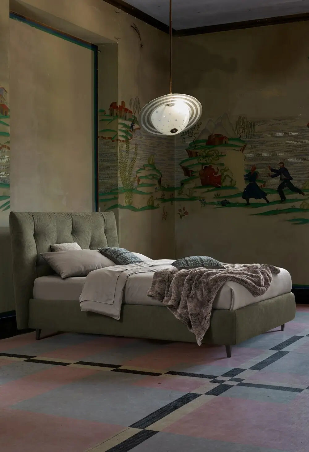 Letto verde oliva con testiera alta e biancheria chiara, posizionato in una stanza con affreschi murali e lampadario moderno