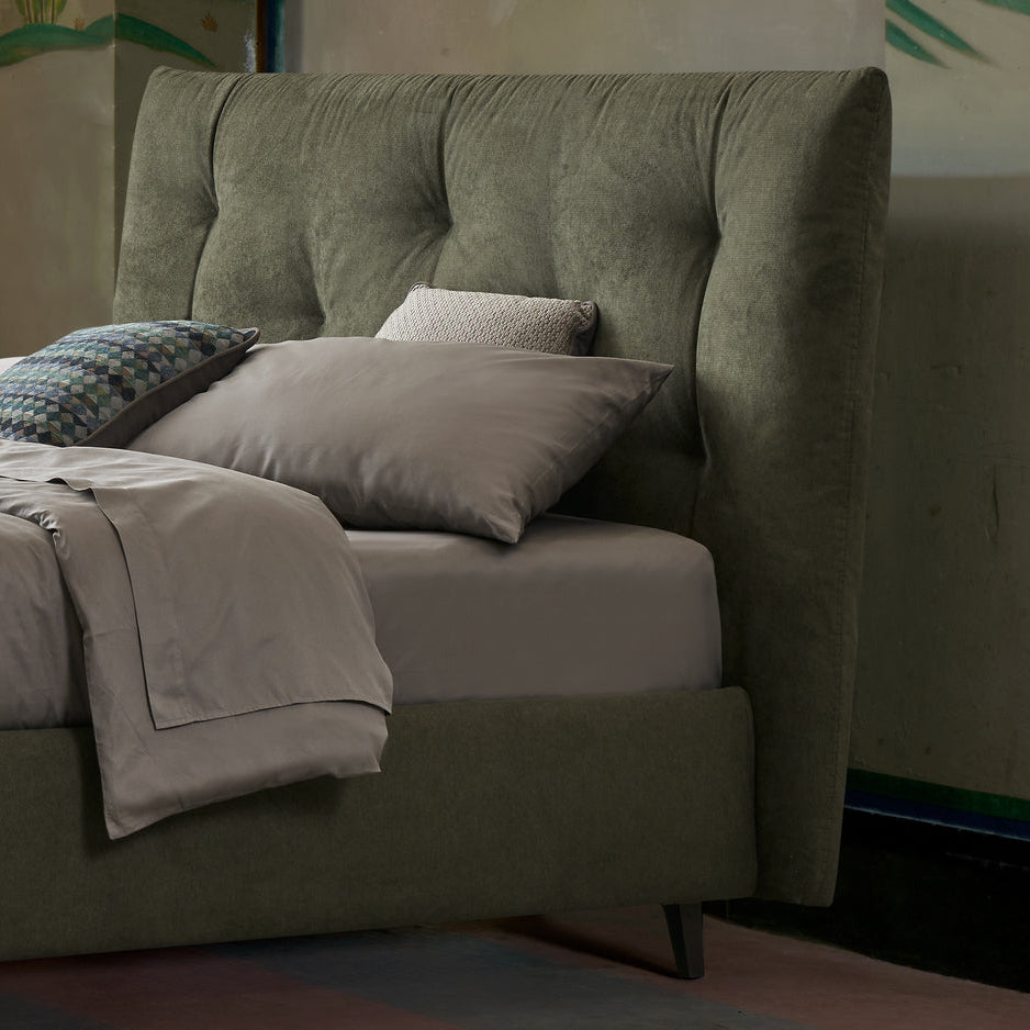 Letto imbottito contenitore verde oliva con testiera trapuntata, lenzuola grigie e cuscini decorativi in una camera elegante e moderna