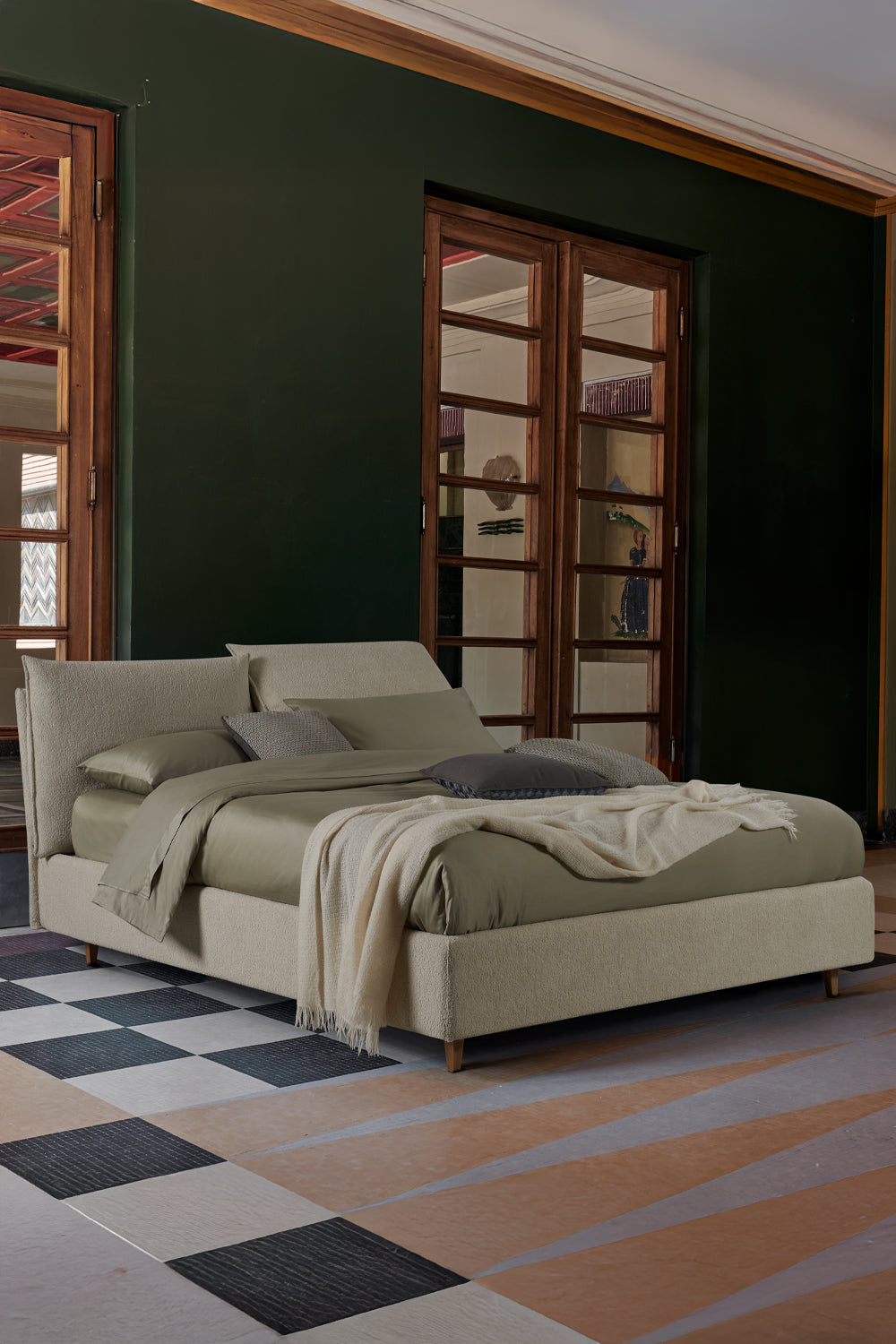 Letto beige con lenzuola tono su tono in una camera luminosa con pareti verde scuro e pavimento a scacchi