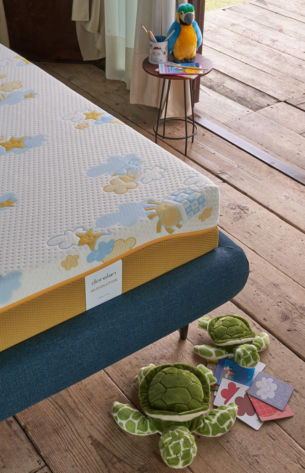 un materasso con i disegni gialli e azzurri di nicoletta costa, in una cameretta con giochi e peluche