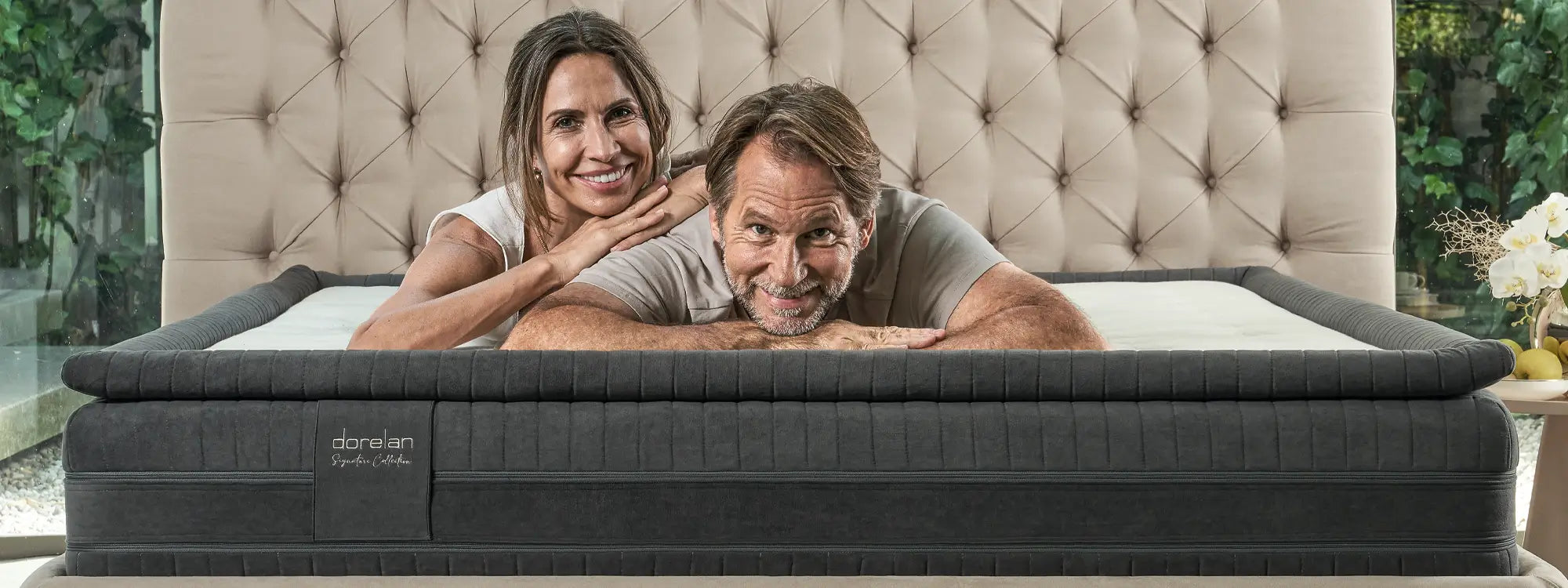 Coppia sorridente distesa su materasso Dorelan, testiera capitonné, comfort e qualità della NUOVA Signature Collection