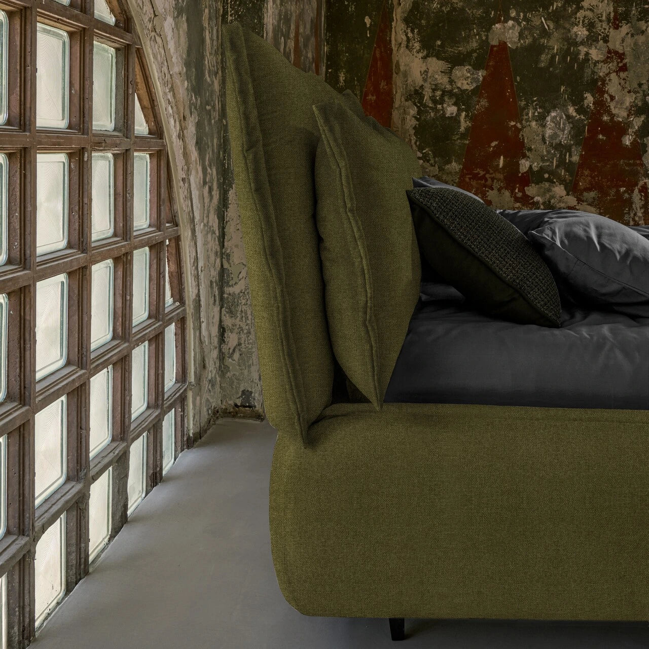 particolare letto di profilo con due cuscinature color verde foresta e lenzuola grigie in stanza marmorea.