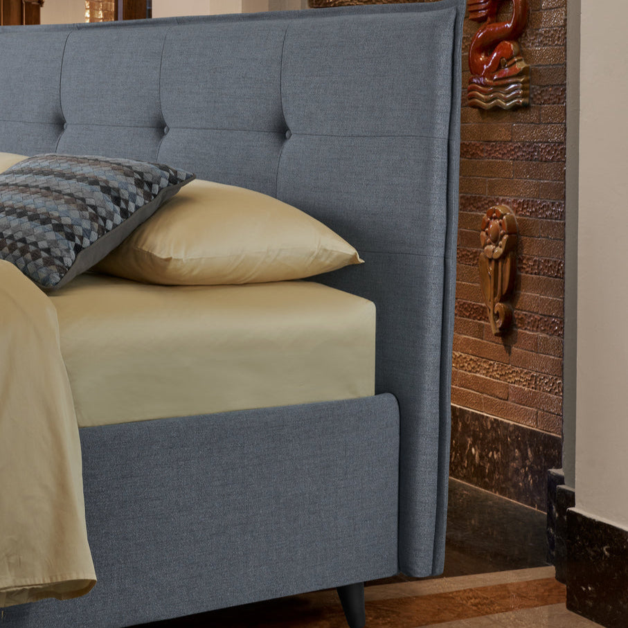 letto azzurro con testiera compatta e impunturata, adatto a spazi ristretti, con lenzuola crema