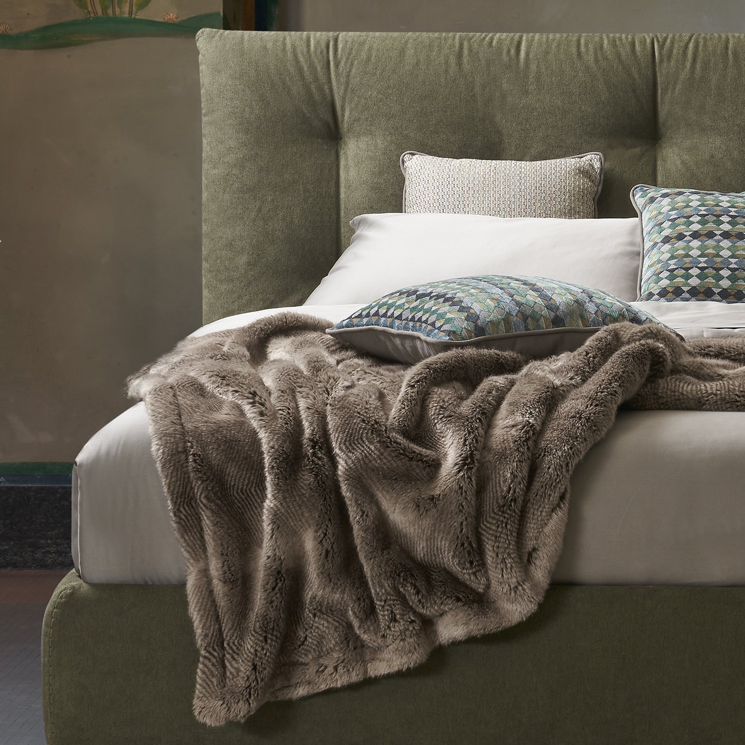 letto verde imbottito con testiera impunturata e lenzuola color crema. macro dettaglio di una coperta pelosa color marrone e cuscini decorativi