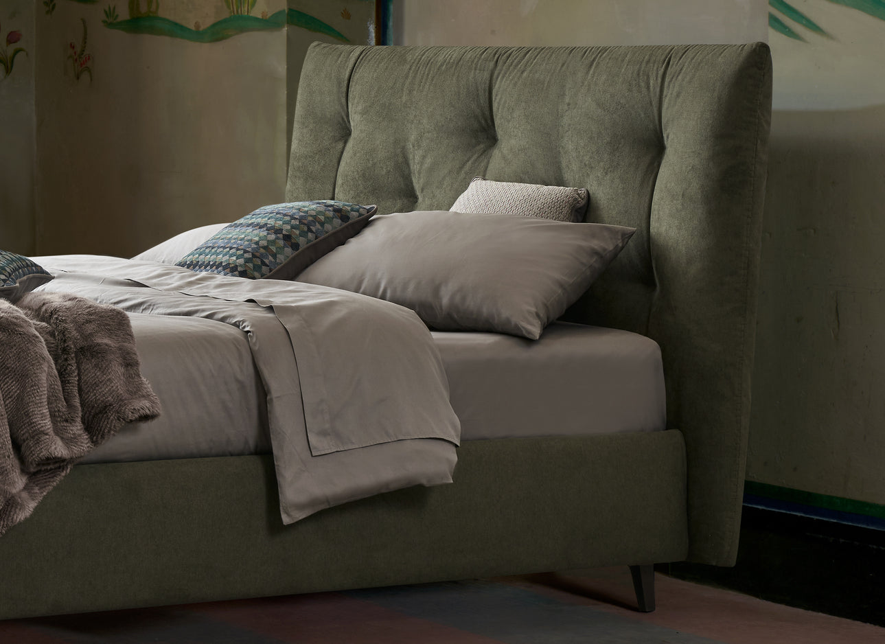 Letto imbottito contenitore verde oliva con testiera trapuntata, lenzuola grigie e cuscini decorativi in una camera elegante e moderna