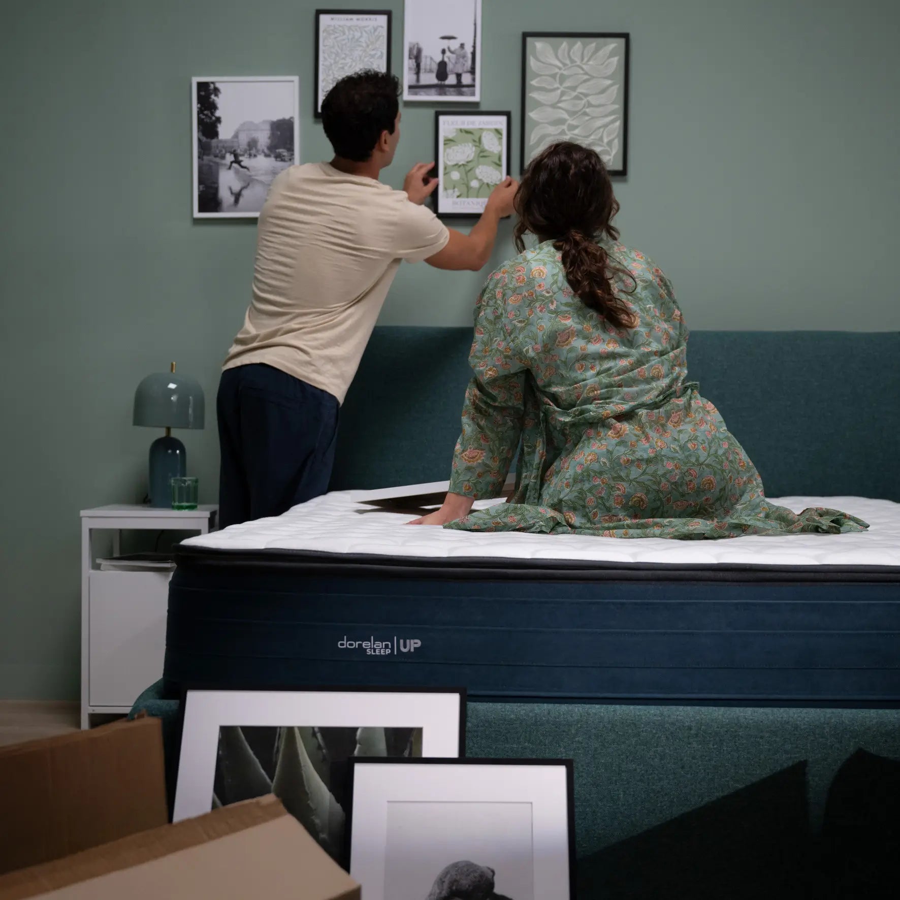 coppia si è appena trasferita in un nuovo appartamento e sta facendo il trasloco. appende quadri sopra al eltto nuovo dorelan